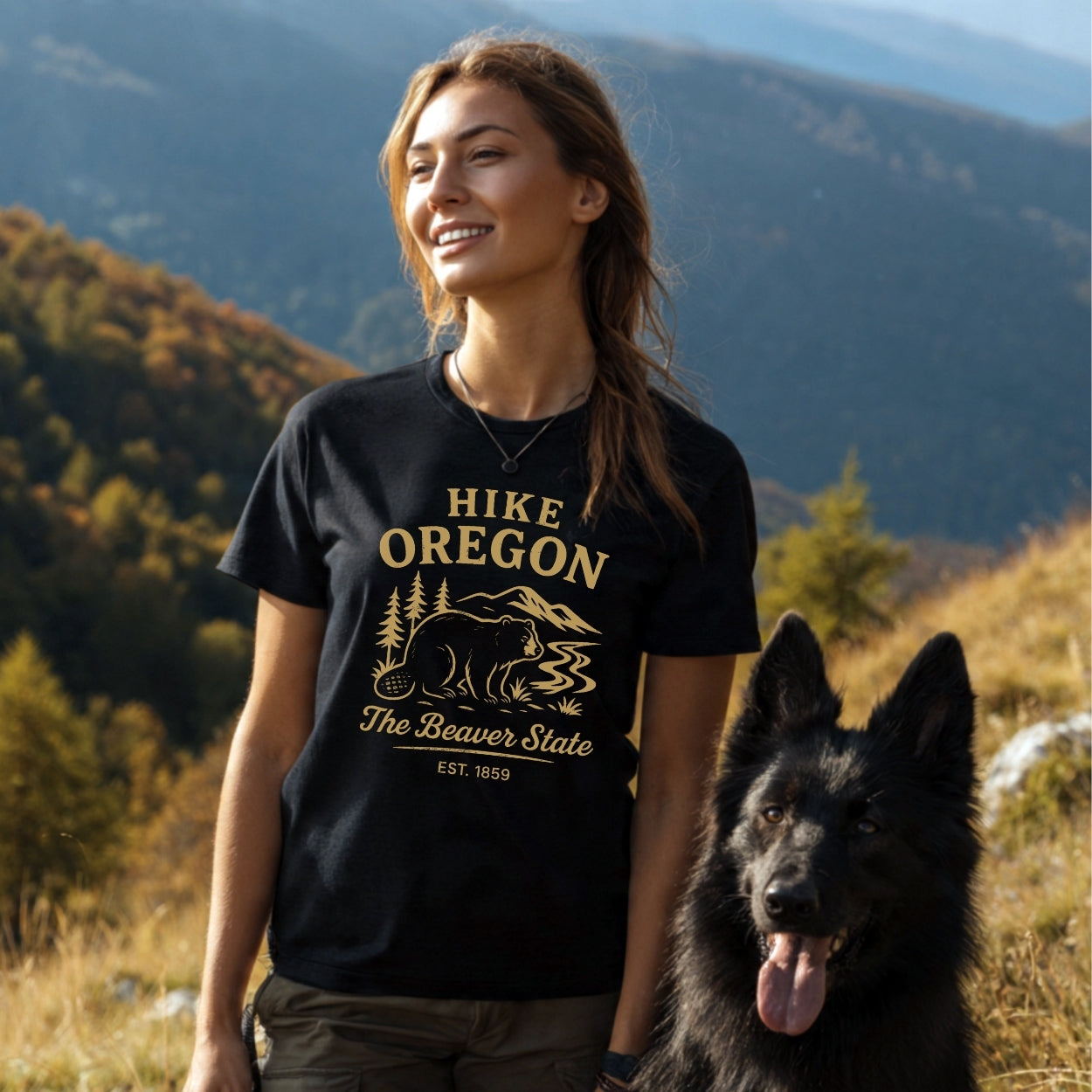 Woman on a forested trail wears the Hike Oregon T-Shirt, featuring durable prints and a comfortable fit. Accompanied by a large dog, they enjoy the scenic autumn backdrop.