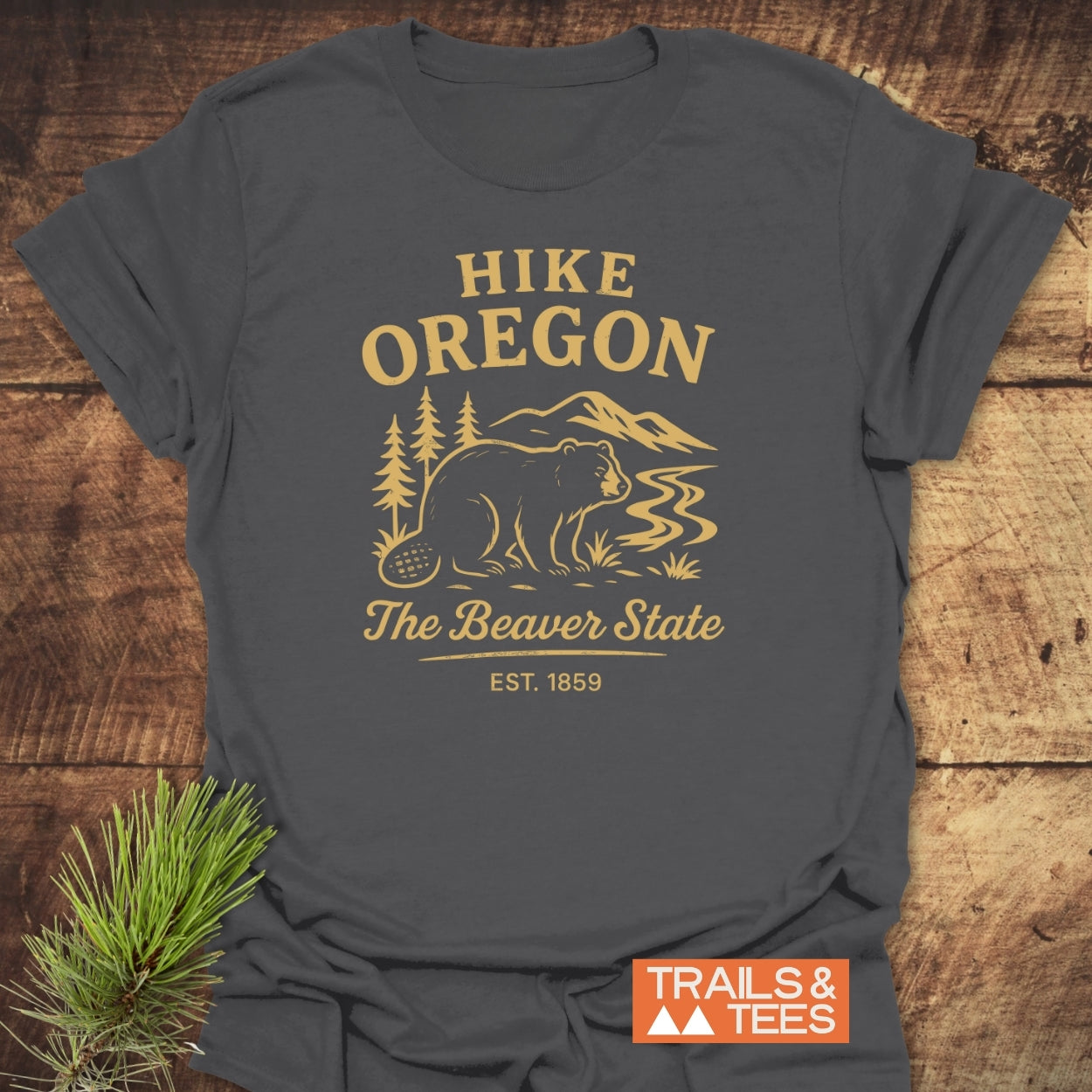 Hike Oregon T-Shirt featuring a stylized outdoor scene with pine trees, a river, and mountains in mustard-yellow. Perfect for everyday adventure, crafted from soft ring-spun cotton for comfort.
