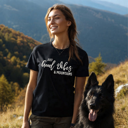 Young woman in a Just Good Vibes & Mountains T-Shirt stands with a large black dog in a hilly, forested autumn landscape, highlighting the tee's outdoor adventure spirit and comfort.