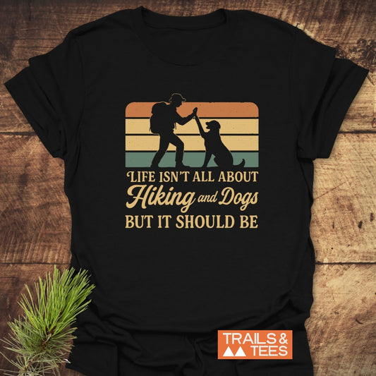 Hiking And Dogs T-Shirt featuring a retro graphic of a backpacker high-fiving a dog against sunset stripes, with the slogan “Life isn’t all about Hiking and Dogs but it should be.”