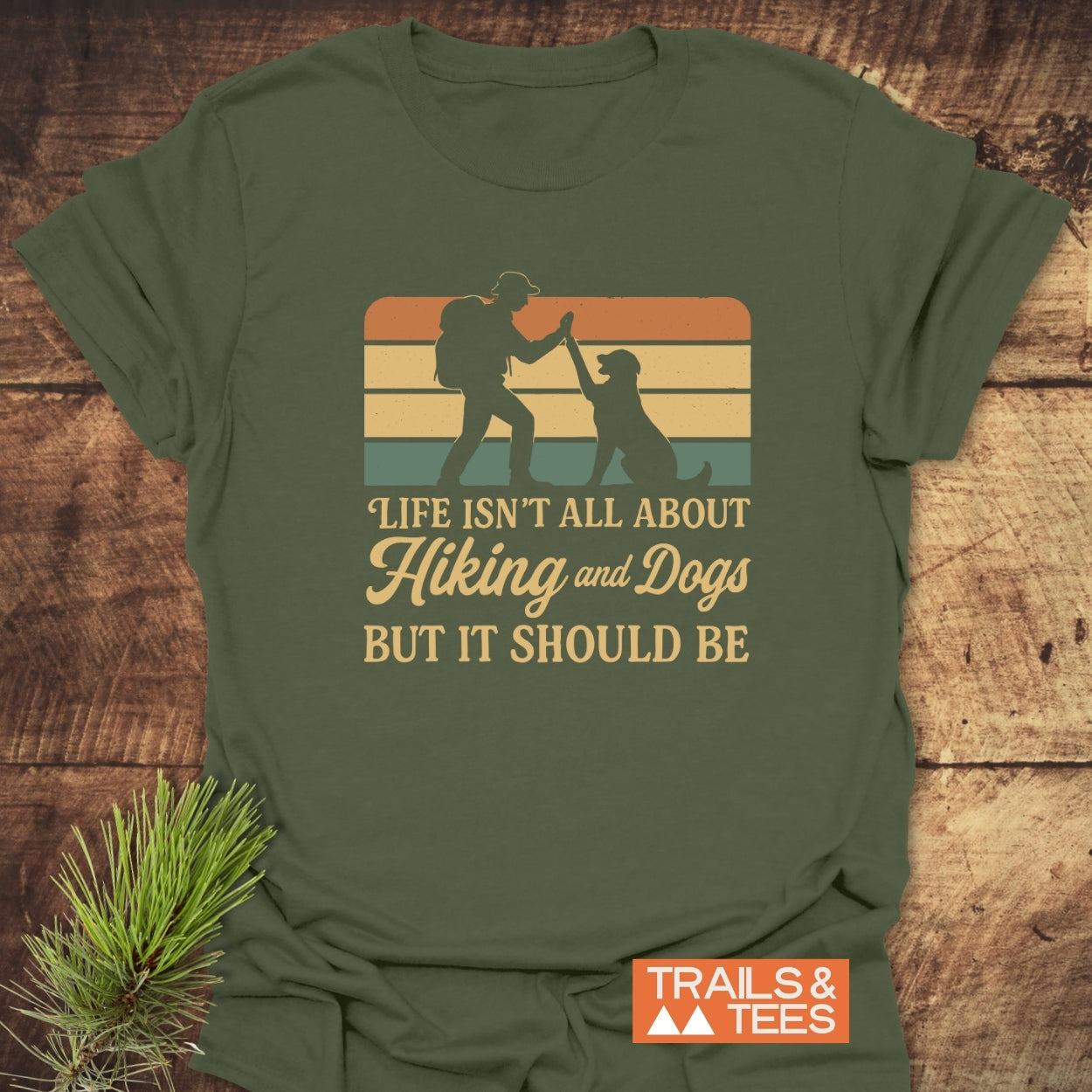 Hiking And Dogs T-Shirt featuring a retro graphic of a hiker and dog high-fiving, set against stripes, slogan below. Crafted from soft cotton for comfort and durability, brand Trails & Tees visible.