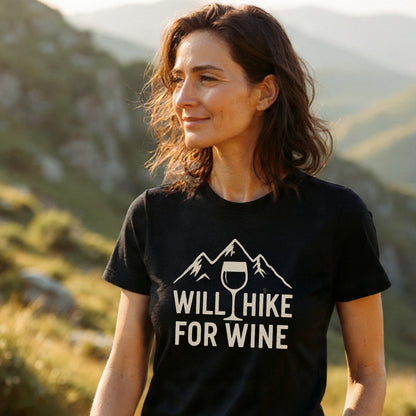 Woman outdoors wearing Will Hike For Wine T-Shirt, featuring a mountain and wine glass design. Made of soft cotton, it's pre-shrunk with durable prints, ideal for outdoor enthusiasts.