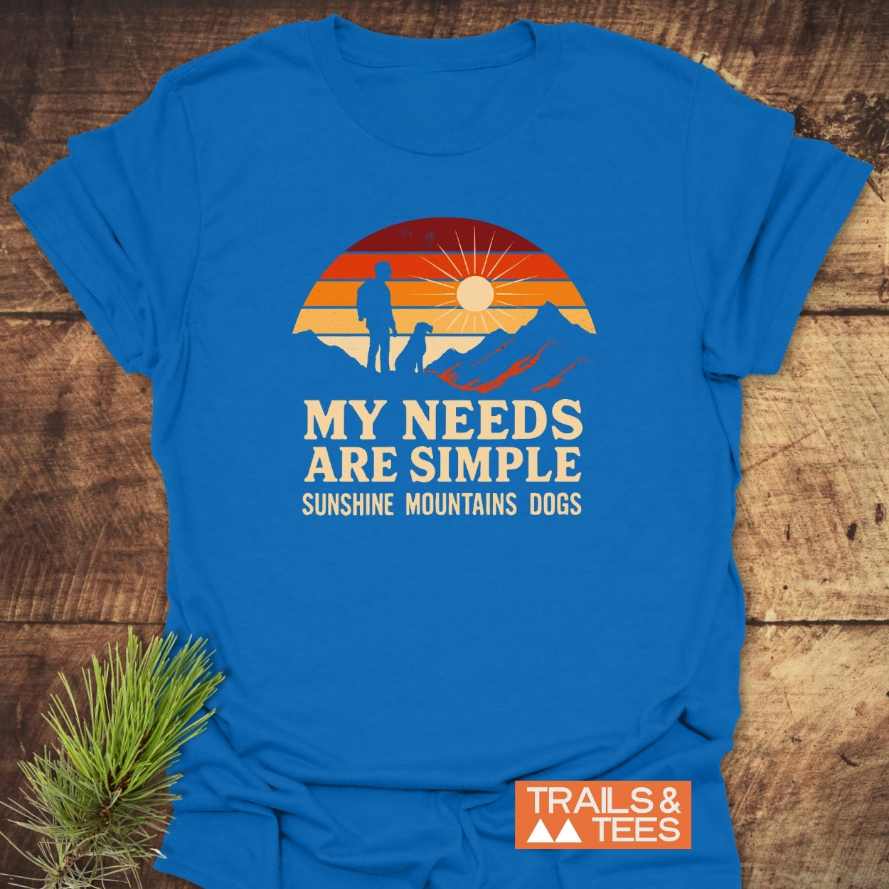 Simple Needs Vintage T-Shirt featuring a graphic of a person and dog against mountains and sunset, with the phrase “MY NEEDS ARE SIMPLE.” Includes Trails & Tees logo, emphasizing outdoor adventure.