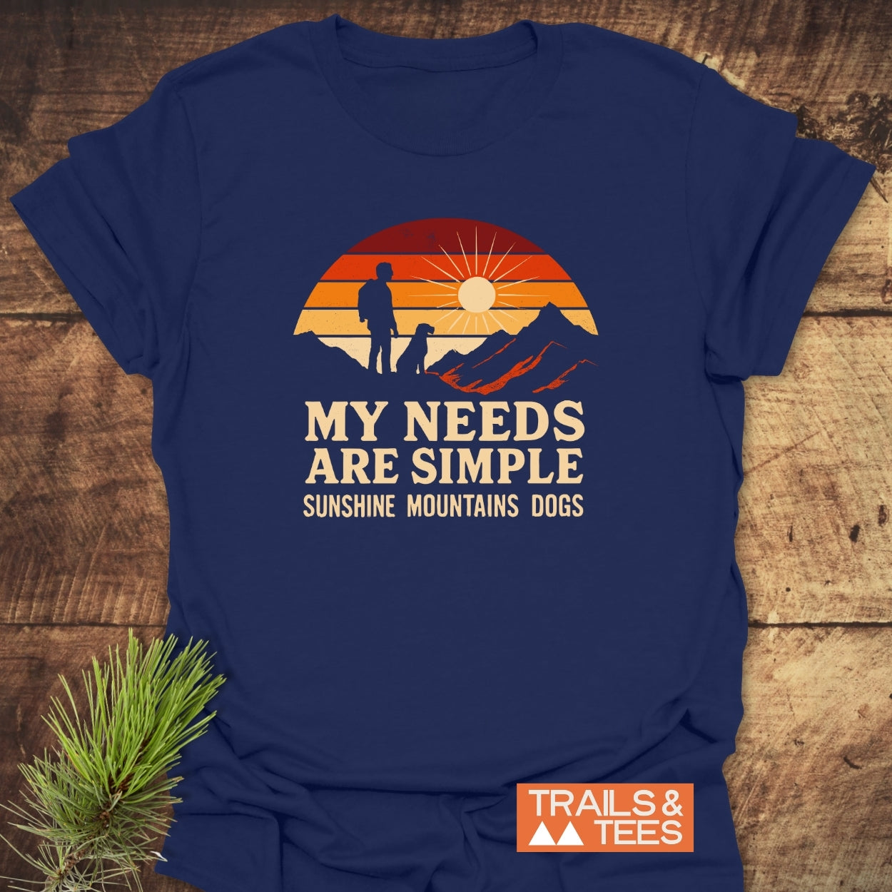 Simple Needs Vintage T-Shirt featuring a retro sunset graphic with a person, dog, and mountains, laid flat. Text reads “MY NEEDS ARE SIMPLE: SUNSHINE, MOUNTAINS, DOGS.” Ideal for outdoor enthusiasts.