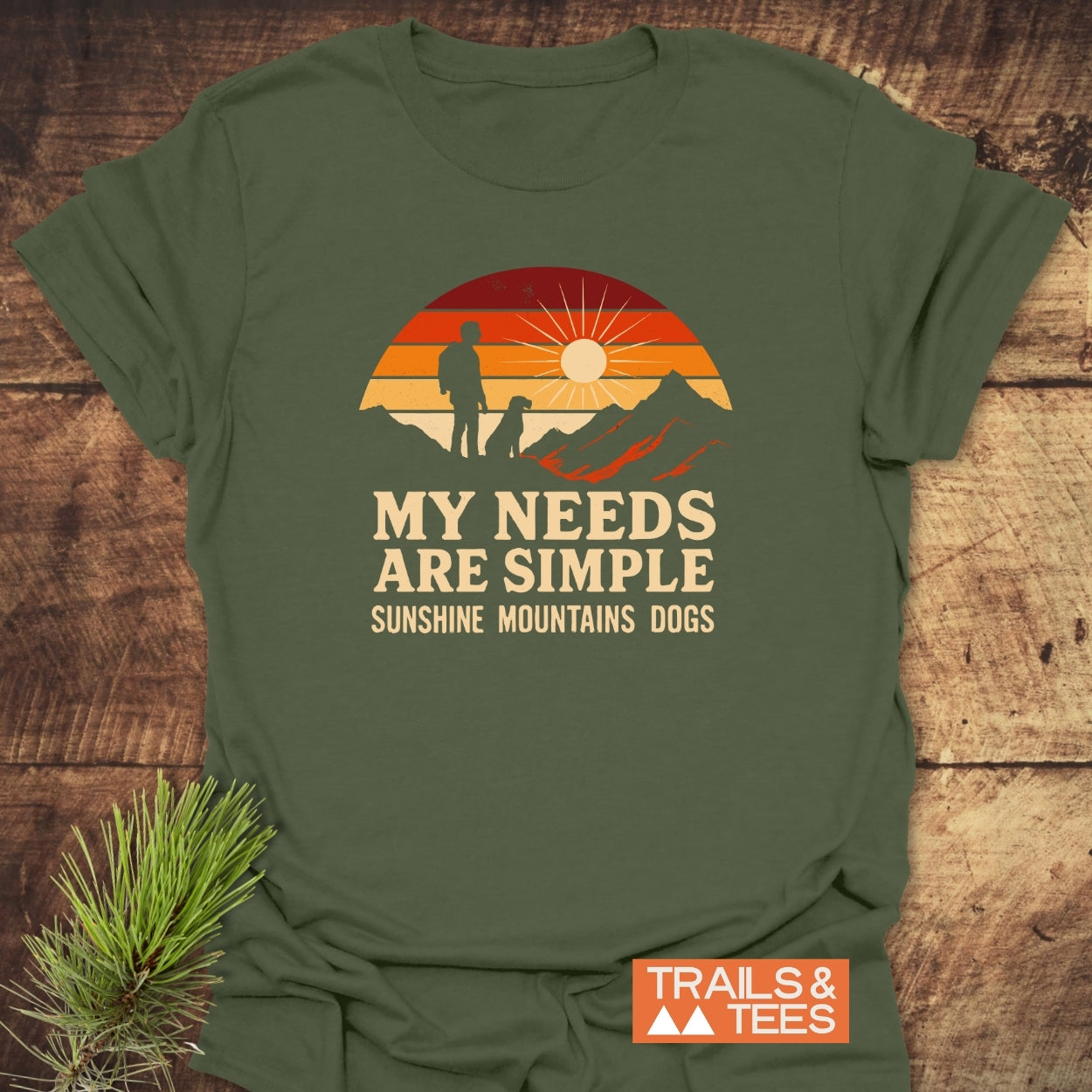 Simple Needs Vintage T-Shirt featuring a retro graphic of a person and dog on a mountain ridge at sunset. Slogan reads, “MY NEEDS ARE SIMPLE: SUNSHINE MOUNTAINS DOGS.” Includes TRAILS & TEES logo.