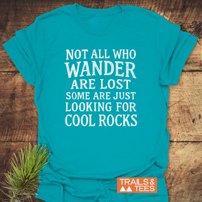 The Not All... Rustic Chalkboard T-Shirt features a bold white slogan on a teal tee, laid on wood with a pine sprig, showcasing the Trails & Tees logo for authentic outdoor vibes.