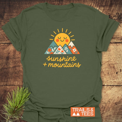 Sunshine And Mountains T-Shirt, featuring a smiling sun and flower-patterned mountains graphic with “sunshine + mountains” slogan. Crafted from ring-spun cotton, it embodies comfort and outdoor-inspired style.