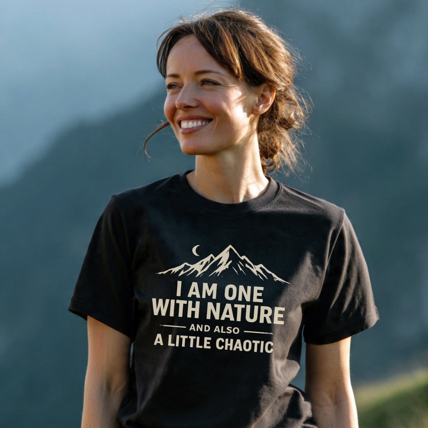 Woman wearing the One With Nature T-Shirt, featuring a mountain range and crescent moon graphic with a playful slogan, highlighting its soft, lightweight cotton ideal for outdoor enthusiasts.