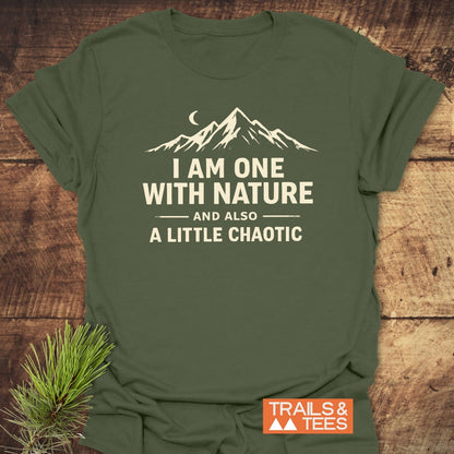 One With Nature T-Shirt featuring a mountain range and crescent moon design, laid on wood with a pine sprig; includes TRAILS & TEES logo, emphasizing adventure-ready comfort and durability.