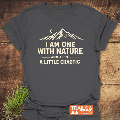 One With Nature T-Shirt showcasing a mountain silhouette and crescent moon design with the phrase I AM ONE WITH NATURE AND ALSO A LITTLE CHAOTIC, featuring the Trails & Tees logo, laid flat.