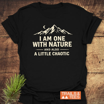 One With Nature T-Shirt, featuring a mountain silhouette and slogan, laid on wood. Includes “TRAILS & TEES.” logo. Designed from soft cotton for comfort, perfect for outdoor enthusiasts.