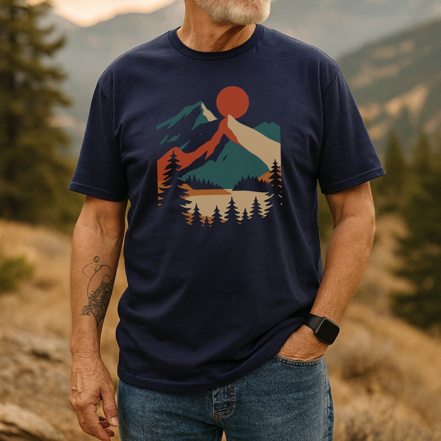 Mountain Sunset Graphic T-Shirt on older man outdoors, featuring a sun, mountains, and pine forest design. Made from soft cotton, it's perfect for everyday adventures. Includes a smartwatch and tattoo detail.