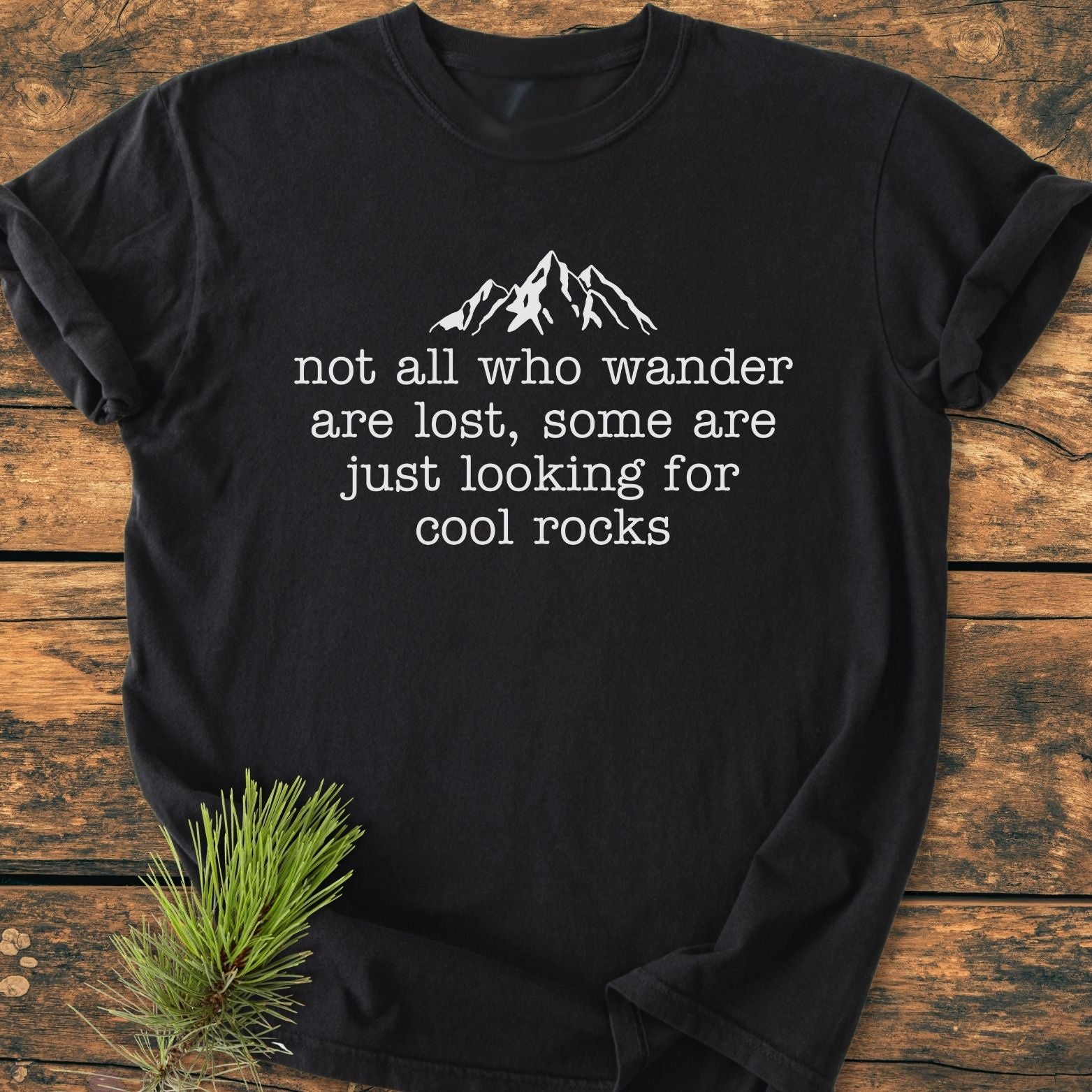 Looking For Cool Rocks Vintage Wash Tee on wooden surface, featuring a mountain silhouette and text. Made of soft, pre-shrunk 100% ring-spun cotton with durable double-needle stitching and a relaxed fit.