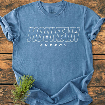 Mountain Energy Vintage Wash Tee on rustic wood, featuring bold white lettering and star accents, complemented by a pine sprig, showcases its soft, durable, pre-shrunk 100% ring-spun cotton fabric.