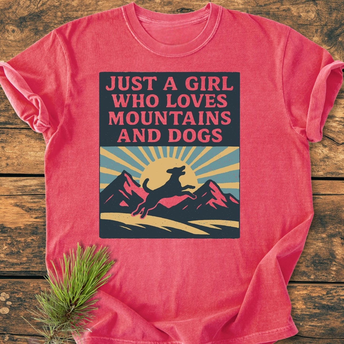 Just A Girl Who Loves Dogs - Vintage Wash Tee features a stylized sunrise and leaping dog graphic, laid on wood with pine sprig, capturing cozy, durable design in soft-washed cotton.