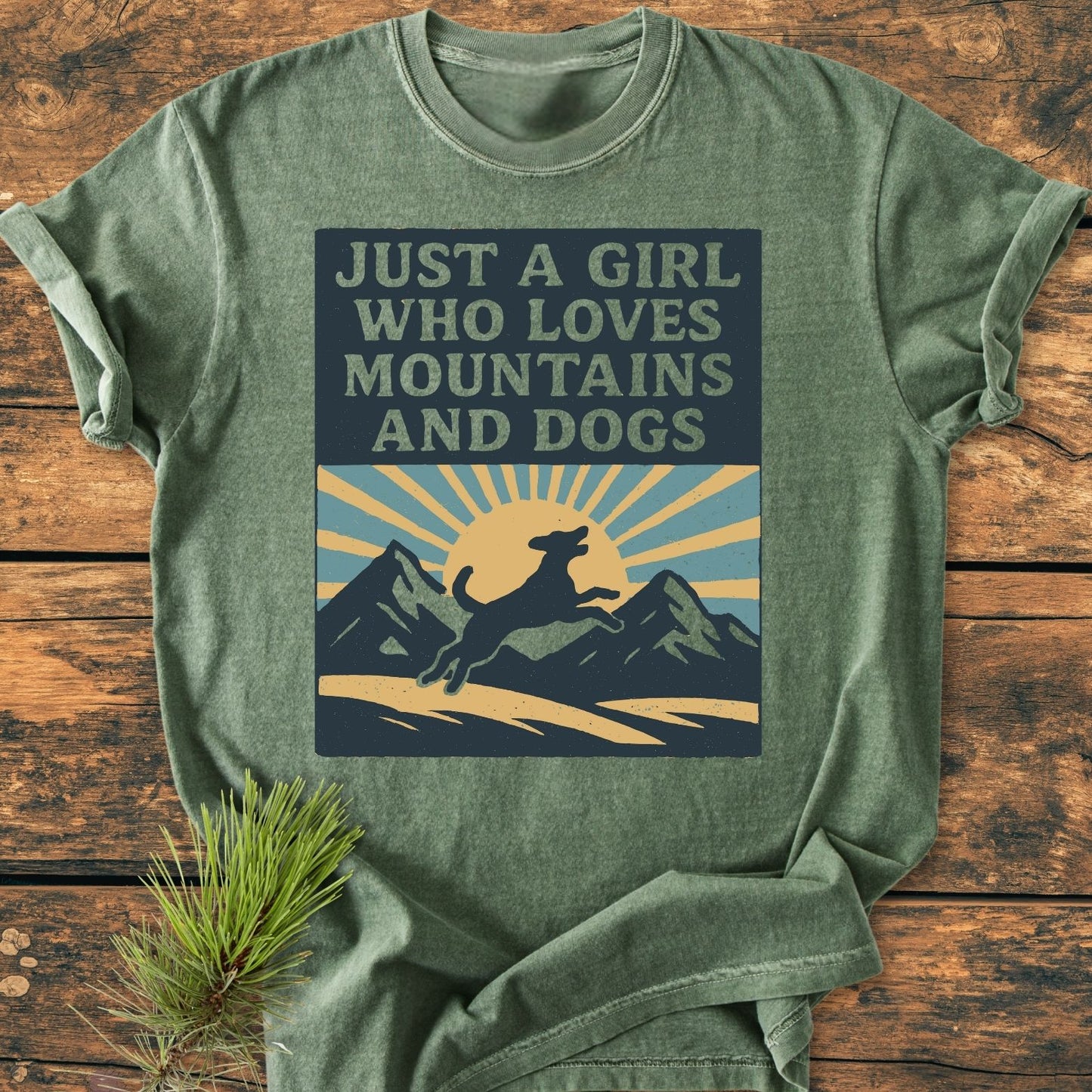 Just A Girl Who Loves Dogs - Vintage Wash Tee featuring a mountain and dog graphic with text, laid on wood with a pine sprig. Made of soft, garment-dyed, 100% ring-spun cotton.