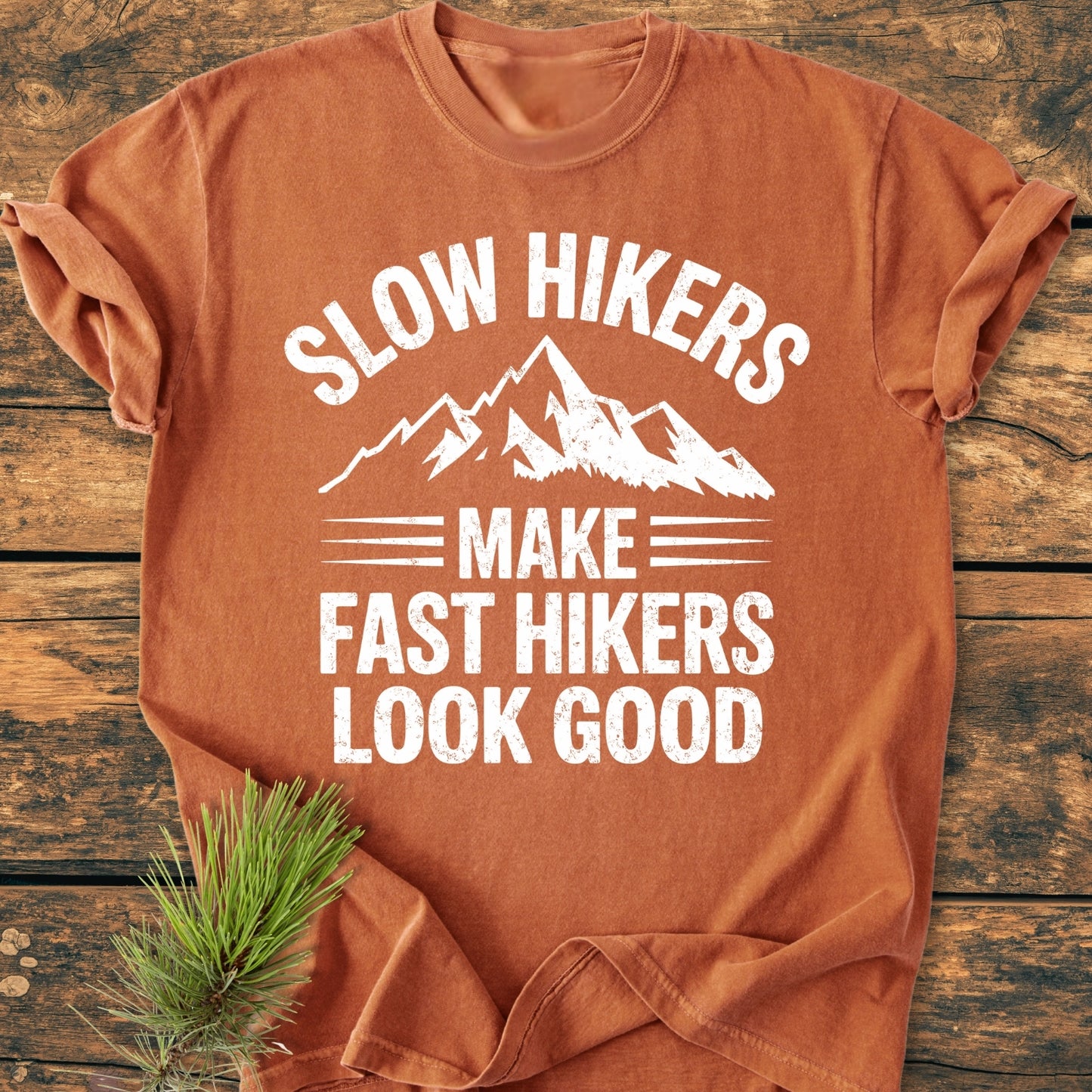 Slow Hikers - Vintage Wash Tee in orange-rust, featuring a white mountain graphic and slogan, laid on rustic wood with pine sprig; 100% ring-spun cotton, relaxed fit, durable stitching.