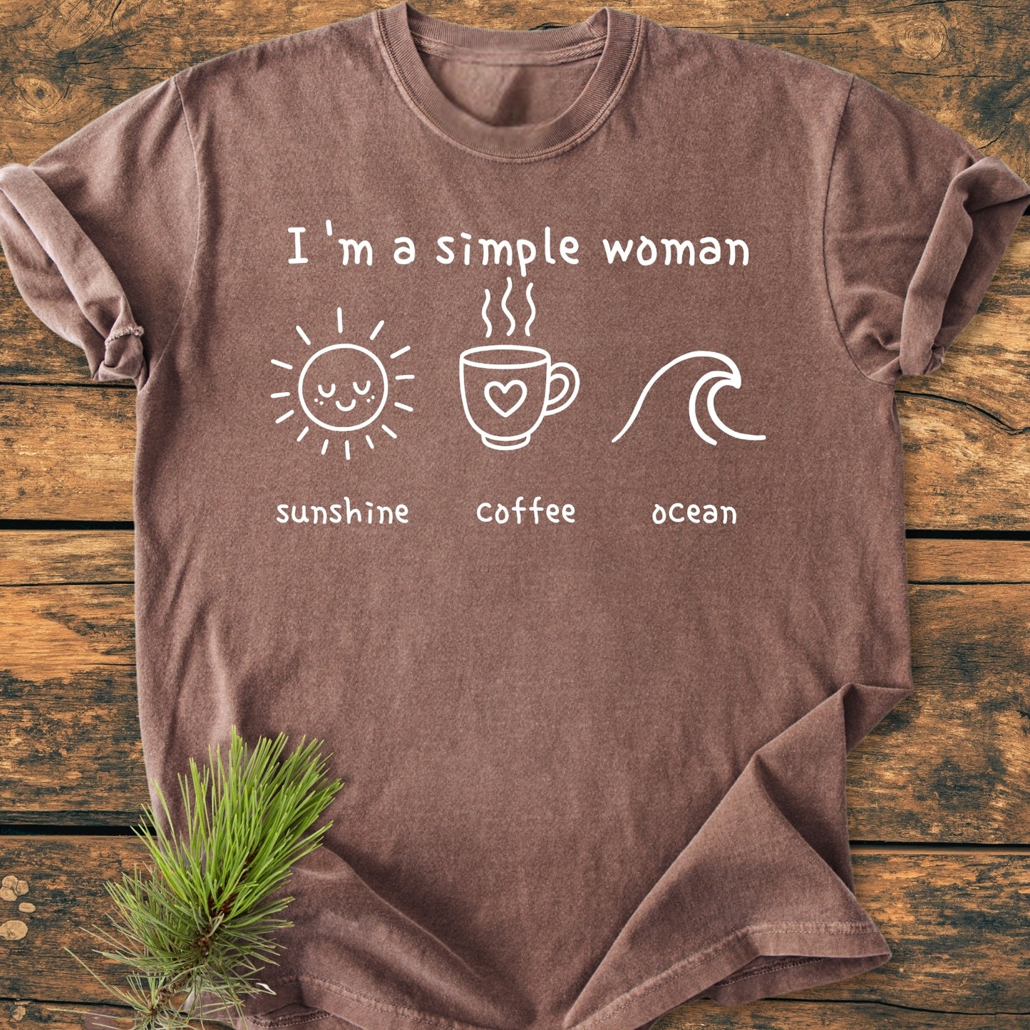 I'm A Simple Woman, Sunshine Coffee Ocean - Vintage Wash Tee features white icons and text on a brown tee, laid on wood with a pine sprig, highlighting its relaxed, garment-dyed design.