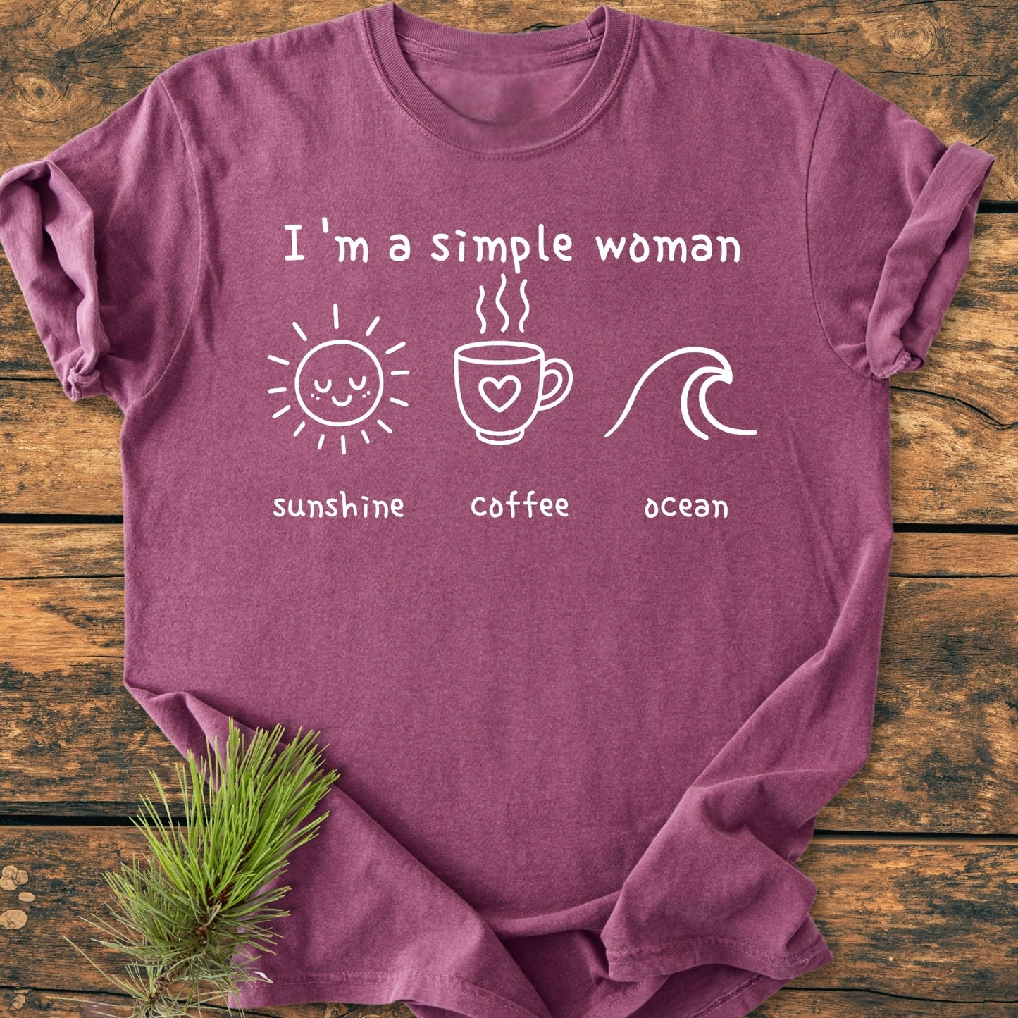 I'm A Simple Woman, Sunshine Coffee Ocean - Vintage Wash Tee features a heather-purple color with a slogan and icons. It lies on wood with a pine sprig, showcasing its relaxed, durable design.