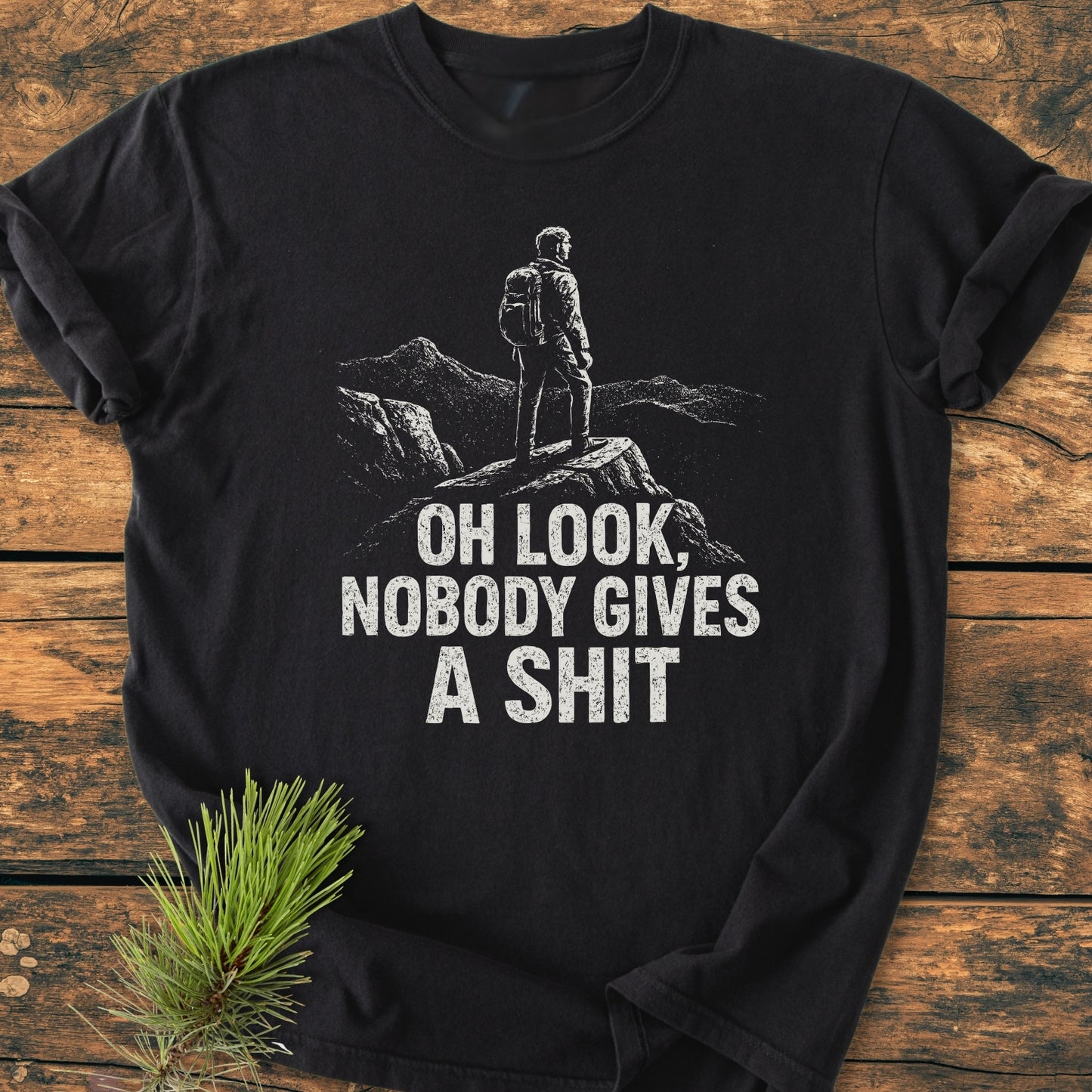 Oh Look - Vintage Wash Tee featuring a sketch-style graphic of a backpacker on a rocky outcrop with distressed text. Laid flat on wood, highlighting its relaxed fit and durable construction.