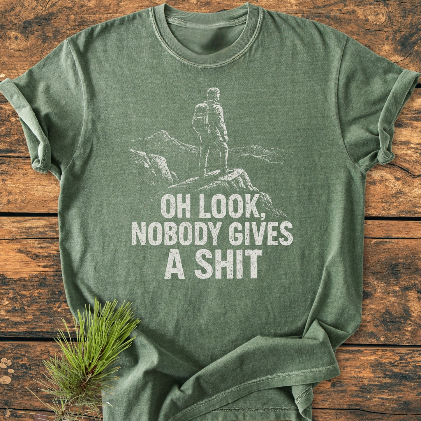 Oh Look - Vintage Wash Tee featuring a white hiker graphic on heather-green, laid flat on wood. Made of soft-washed, ring-spun cotton, this relaxed fit tee offers comfort and durability.