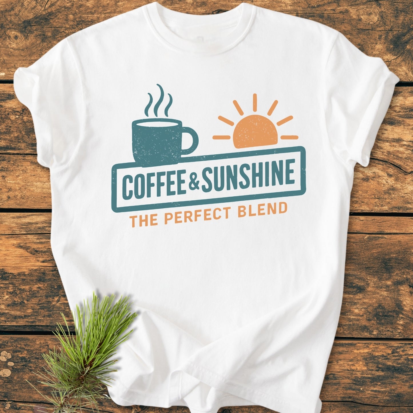 Coffee And Sunshine, Perfect Blend - Vintage Wash Tee featuring a steaming coffee mug and sun graphic with text. Laid flat on wood, accompanied by greenery, showcasing its relaxed fit and durable stitching.