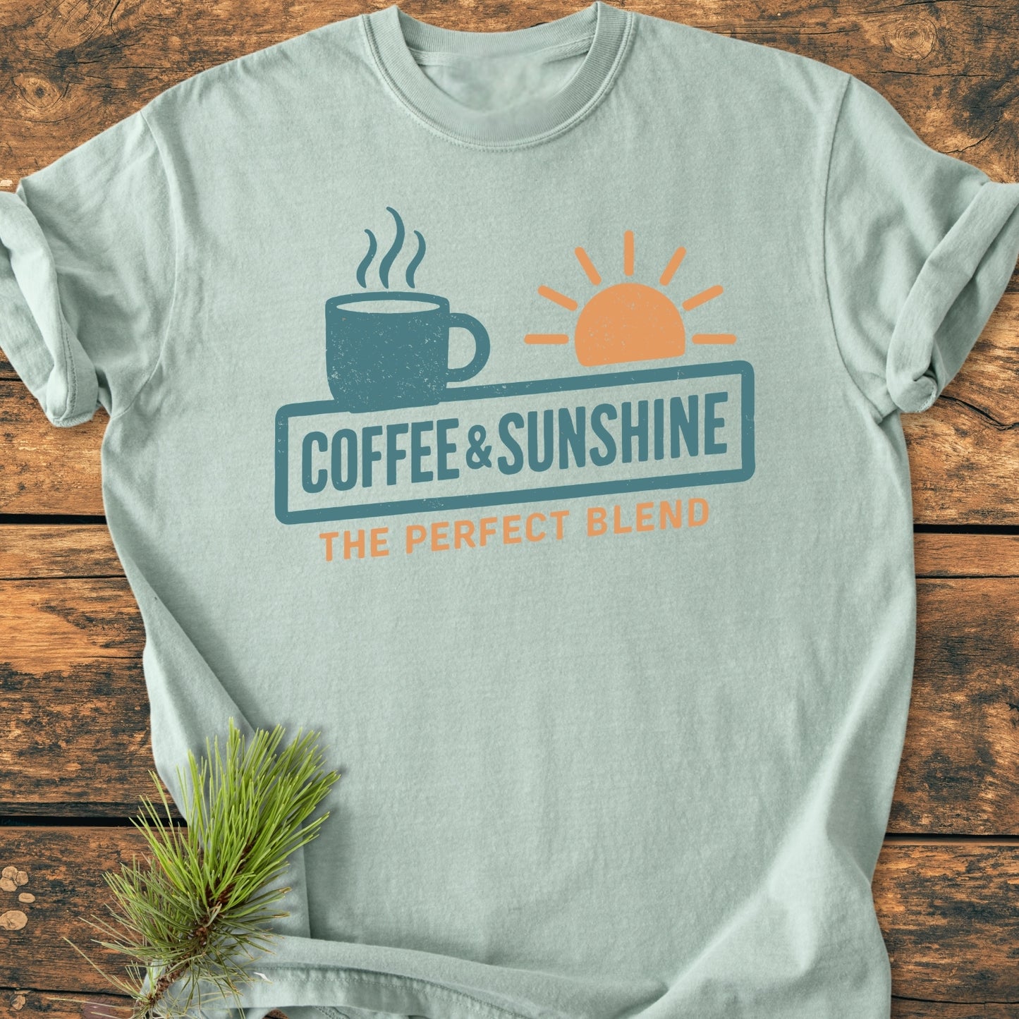 Coffee And Sunshine, Perfect Blend - Vintage Wash Tee, features a retro coffee mug and sun graphic on light-green fabric, styled with a pine sprig, highlighting its cozy, relaxed fit.
