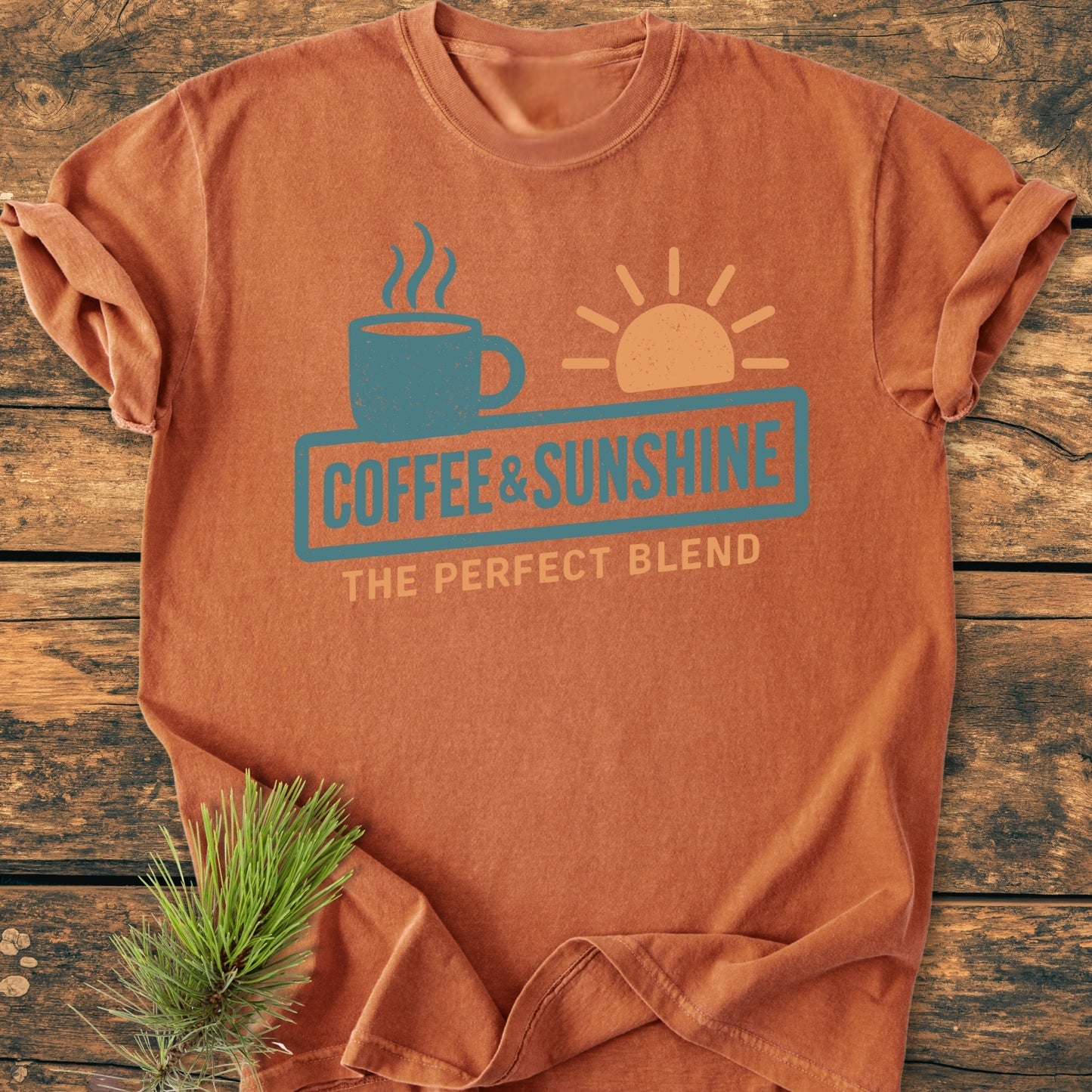 Coffee And Sunshine, Perfect Blend - Vintage Wash Tee: Washed-rust T-shirt with teal coffee cup and pale orange sun graphics, slogan COFFEE & SUNSHINE and THE PERFECT BLEND, on a weathered wooden surface.