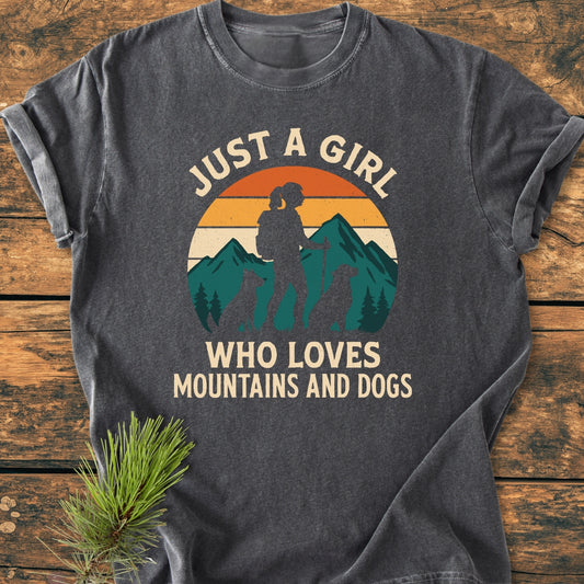 Mountains And Dogs - Vintage Wash Tee: Heather-gray T-shirt with a retro-style sunset graphic, featuring a girl hiker and dogs. Cream text reads “JUST A GIRL WHO LOVES MOUNTAINS AND DOGS.”