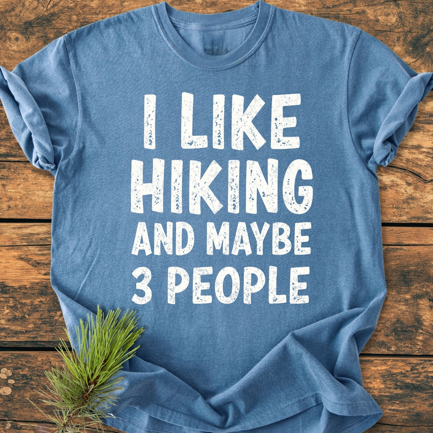Heather-blue I Like Hiking And Maybe 3 People - Vintage Wash Tee with distressed white print on a wooden surface, featuring a pine branch accent. Relaxed fit, 100% ring-spun cotton.