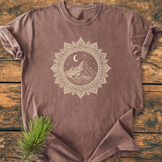 Mountain Mandala - Vintage Wash Tee featuring a hand-drawn mountain scene within a mandala on soft, washed-out brown fabric, laid flat on wood with a pine sprig accentuating the rustic charm.