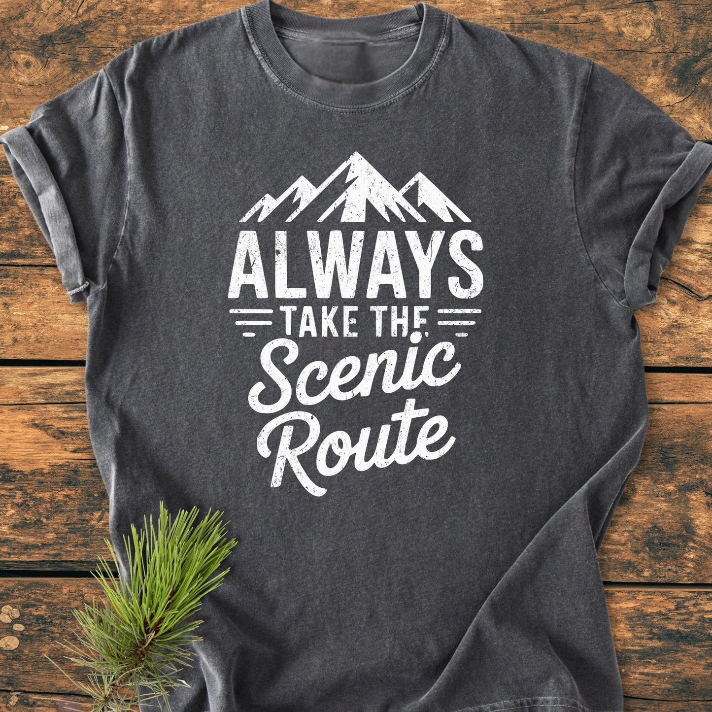 Always Take The Scenic Route - Vintage Wash Tee in charcoal-gray with mountain graphic and slogan on a rustic wooden surface, featuring soft-washed, garment-dyed cotton for a relaxed fit.