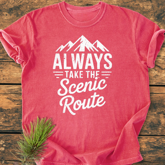 Always Take The Scenic Route - Vintage Wash Tee displayed flat with a white mountain graphic and slogan. Soft heathered fabric and relaxed fit showcased, enhanced by a pine sprig beside it.