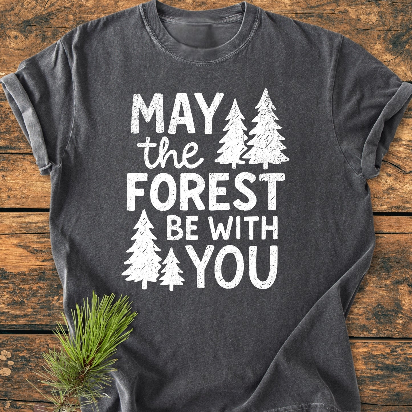 May The Forest Be With You - Vintage Wash Tee, featuring a Star Wars-inspired slogan with evergreen trees, laid on wood; 100% ring-spun cotton for comfort and durability, accented with a pine sprig.