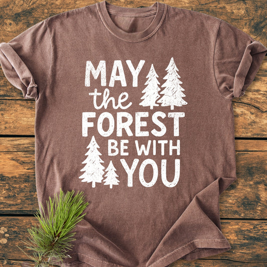 Folded May The Forest Be With You - Vintage Wash Tee with white slogan and pine-tree silhouettes on brown fabric, styled with a pine sprig; showcases Comfort Colors' soft, relaxed fit, garment-dyed cotton shirt.