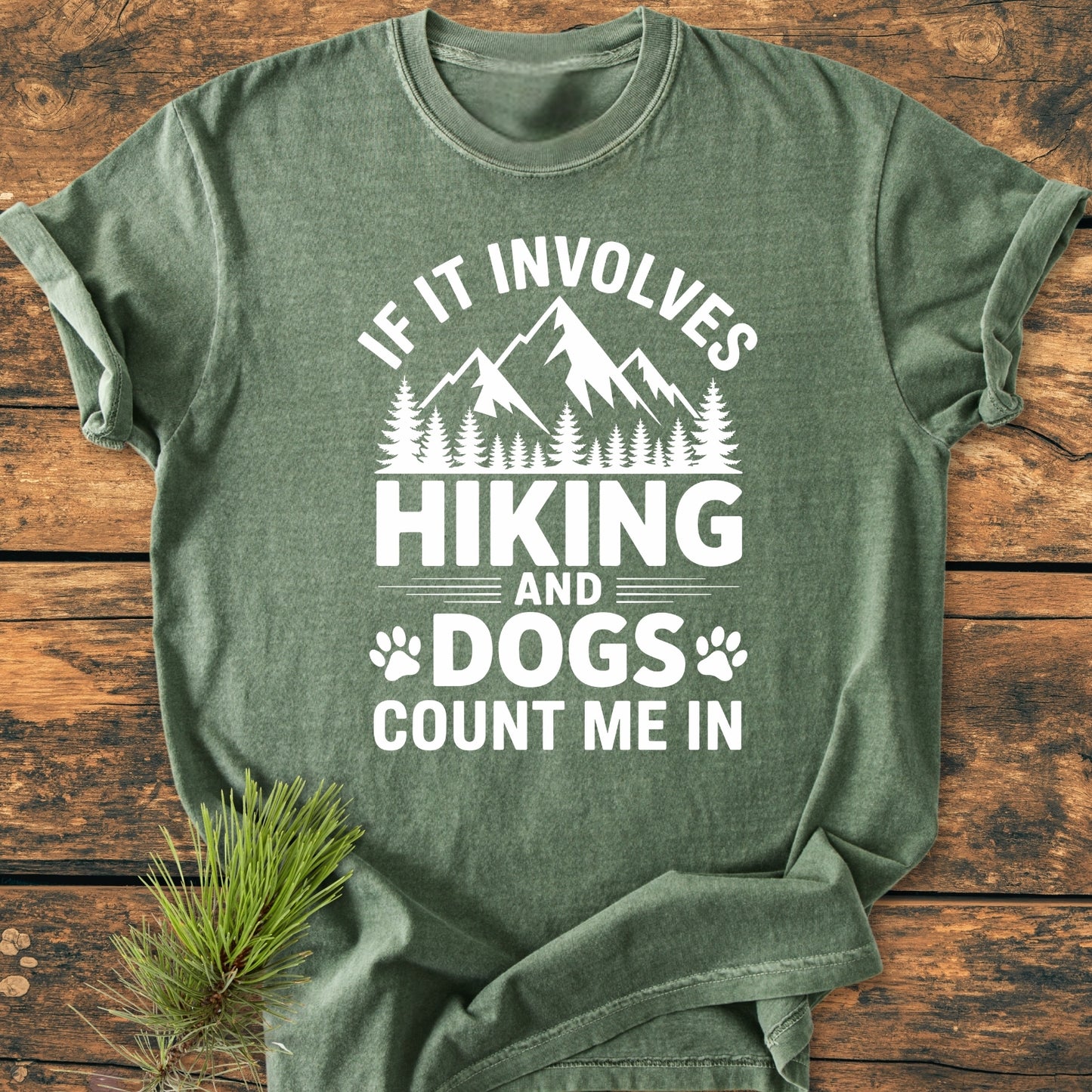 Heather-green Hiking And Dogs - Vintage Wash Tee on rustic wood, featuring a mountain range, pine trees, and paw icons. Cozy, relaxed fit, pre-shrunk cotton with durable stitching and tubular shape retention.