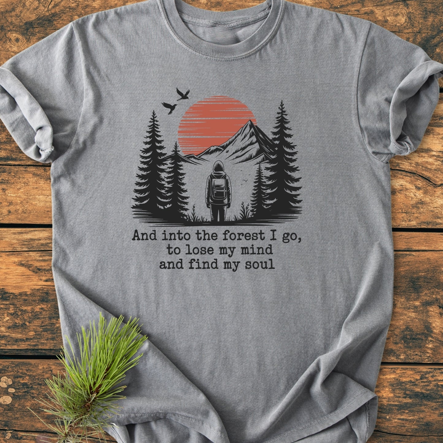 And Into The Forest I Go - Vintage Wash Tee features a backpacker graphic amid trees and mountains with a quote, on a heather-gray T-shirt, showcasing a relaxed fit and soft-washed fabric.