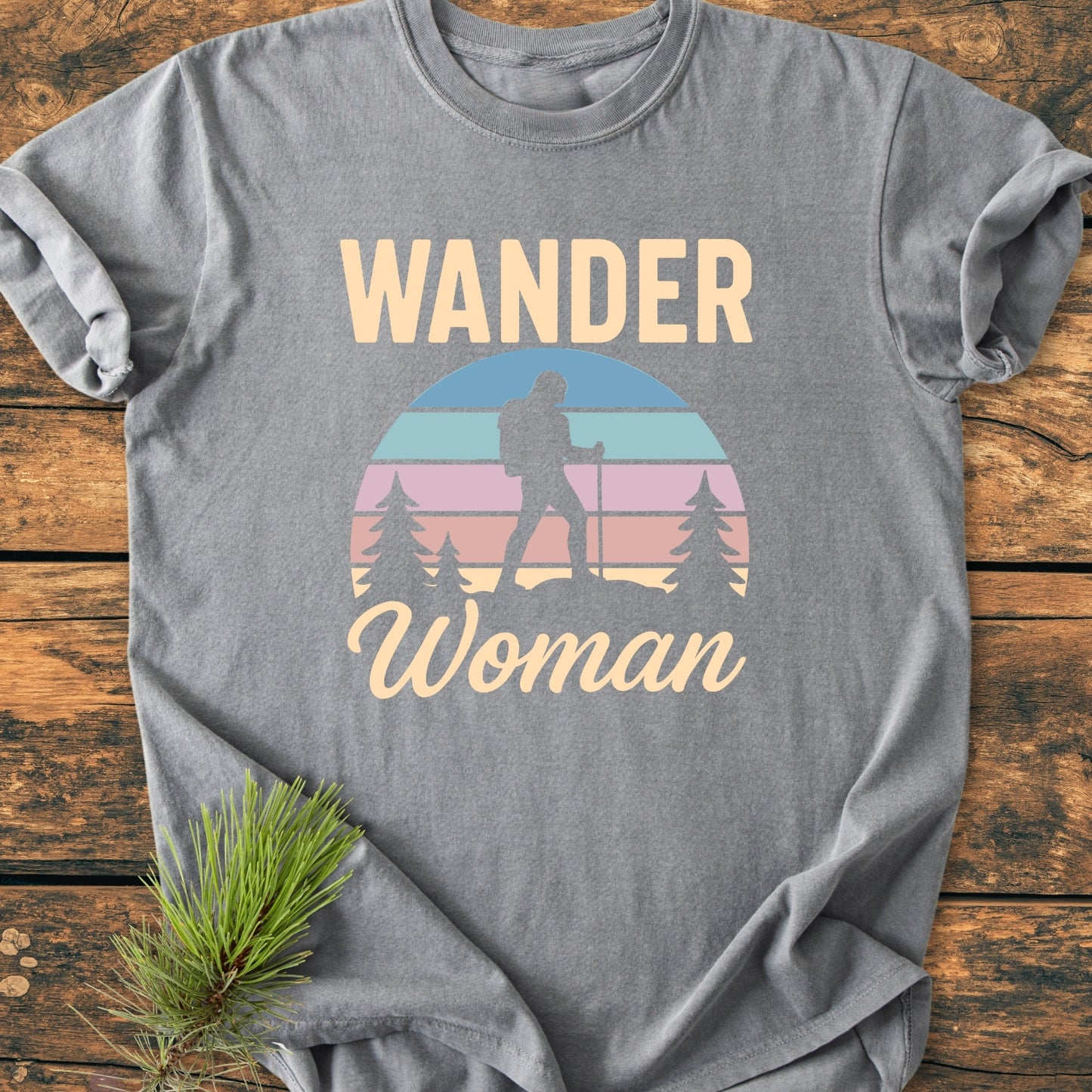 Wander Woman Retro - Vintage Wash Tee features a heather-gray design with a WANDER graphic and backpacker silhouette. Laid on wood, it showcases a relaxed fit and durable stitching.