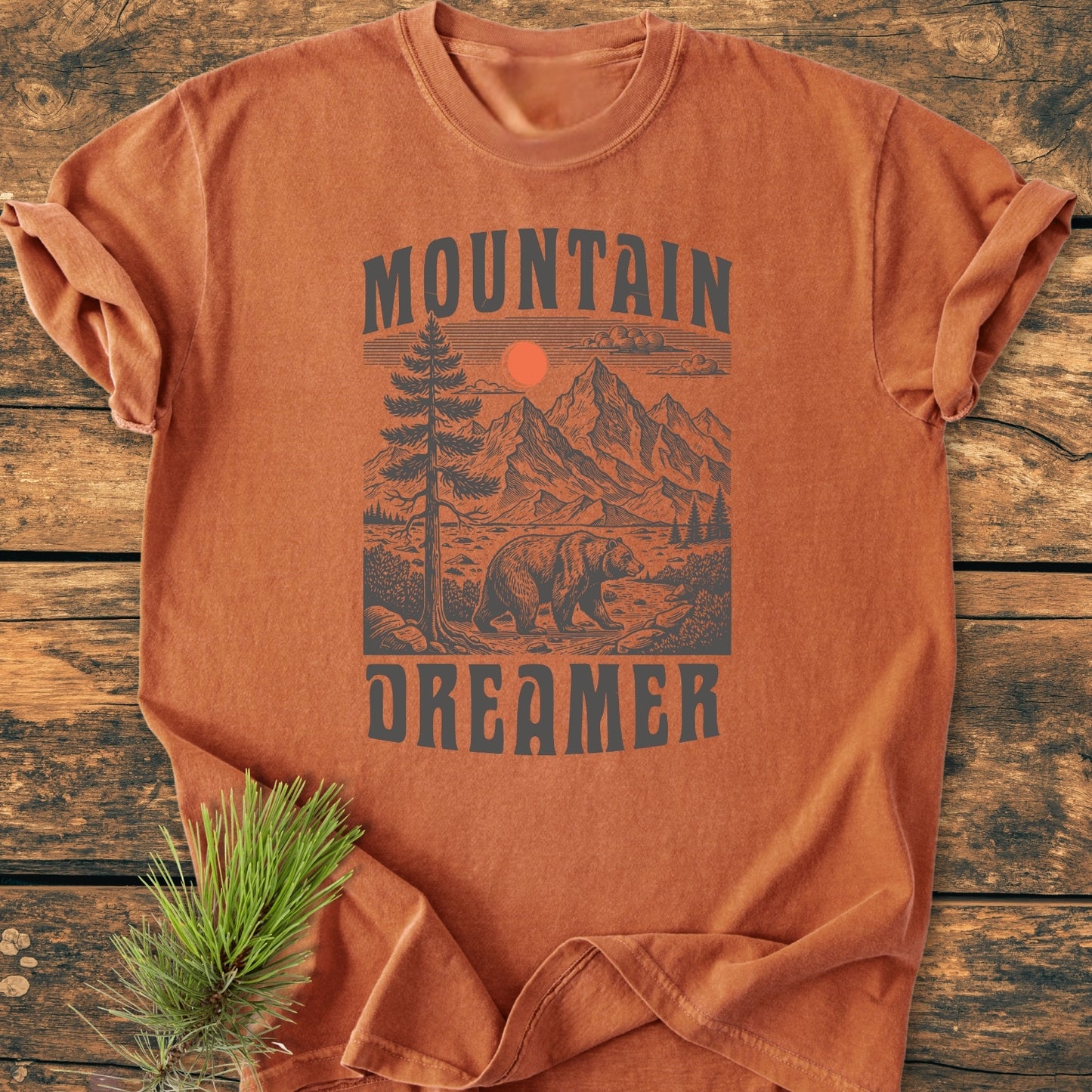 Mountain Dreamer - Vintage Wash Tee features a heather-gray wilderness print on a rust T-shirt, showcasing rugged mountains, a pine, sun, and bear, presented on a cozy, relaxed-fit garment.