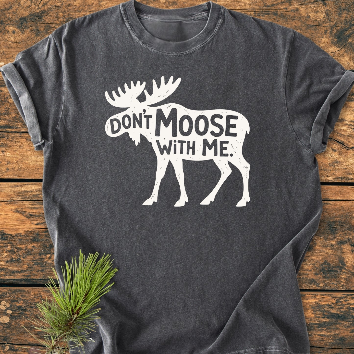 Don't Moose With Me - Vintage Wash Tee features a white moose silhouette with a playful slogan on a soft, charcoal-gray fabric, laid on wood with pine accent, highlighting comfort and durability.