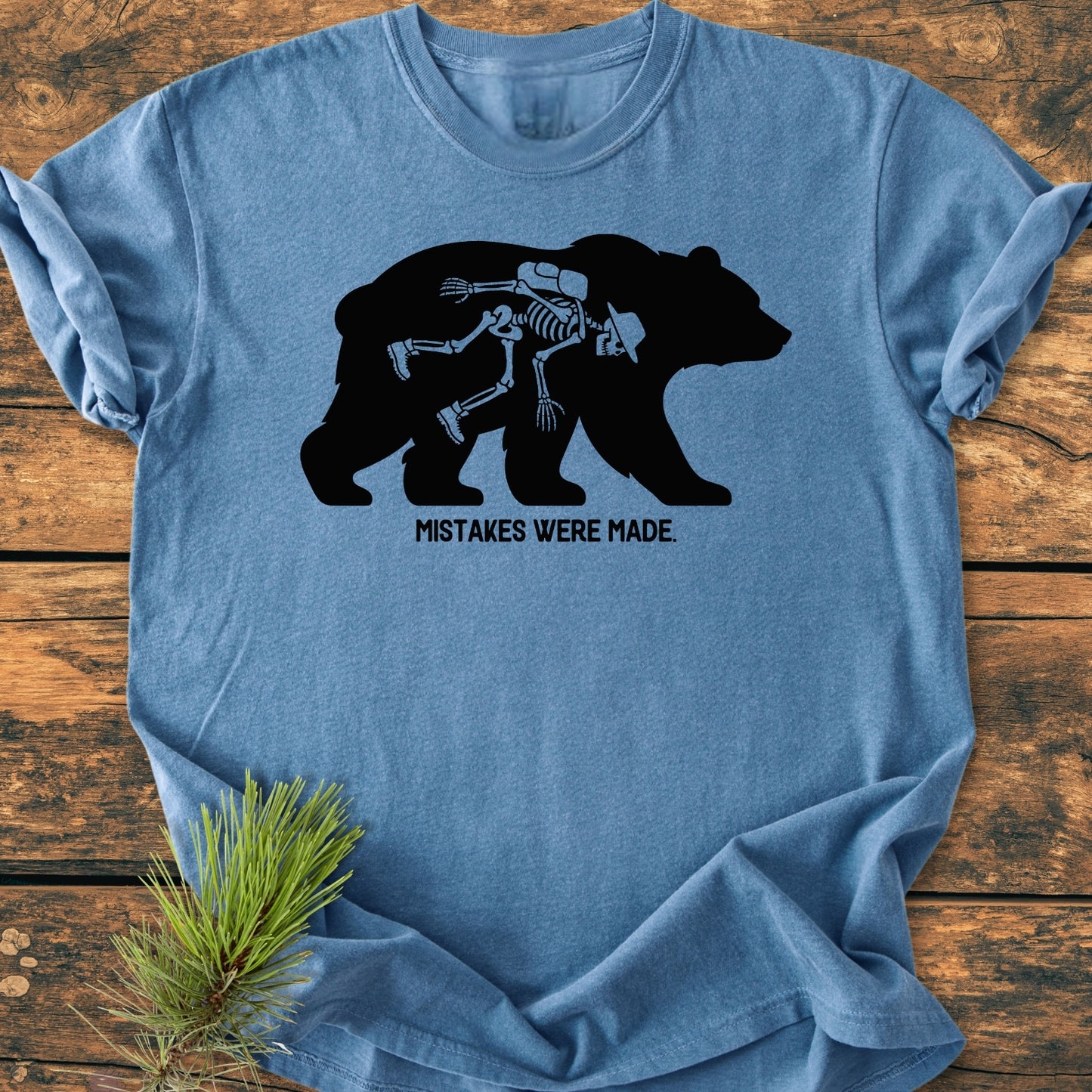 Mistakes Were Made - Vintage Wash Tee featuring a black bear silhouette with a human skeleton inside, laid on wood with pine sprig, offers a relaxed fit and durable design in blue-heather.