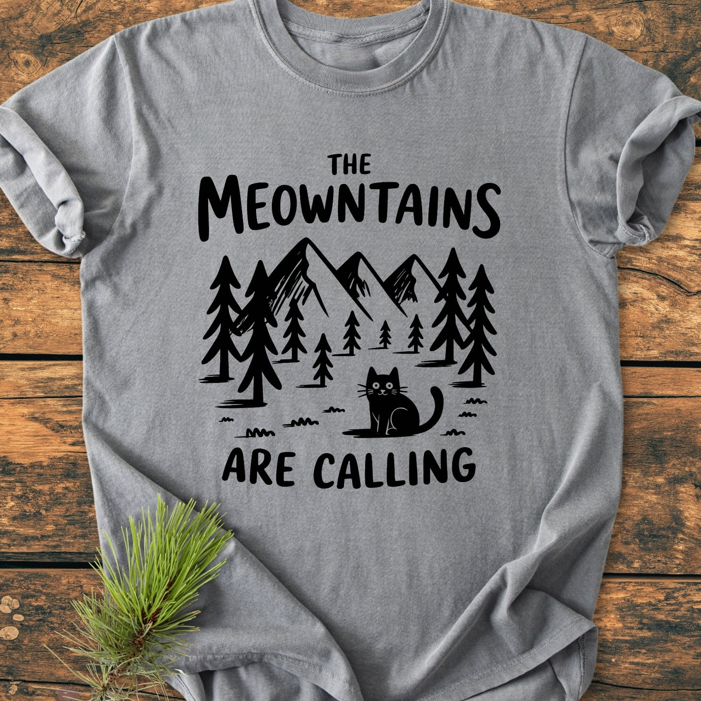The Meowntains Are Calling - Vintage Wash Tee features a mountain scene with a cartoon cat, printed on heather-gray fabric, showcasing its relaxed fit and cozy texture.