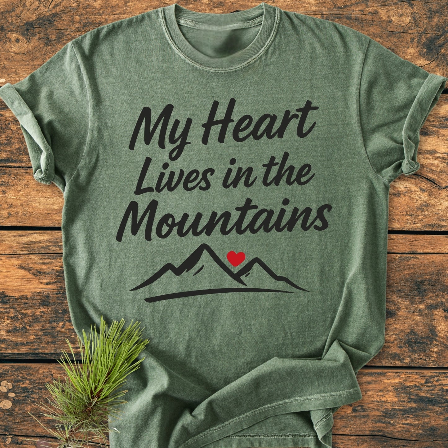 My Heart Lives In The Mountains - Vintage Wash Tee, a heather-green T-shirt, features mountain artwork and script on a rustic surface, embodying cozy, garment-dyed comfort and relaxed fit.