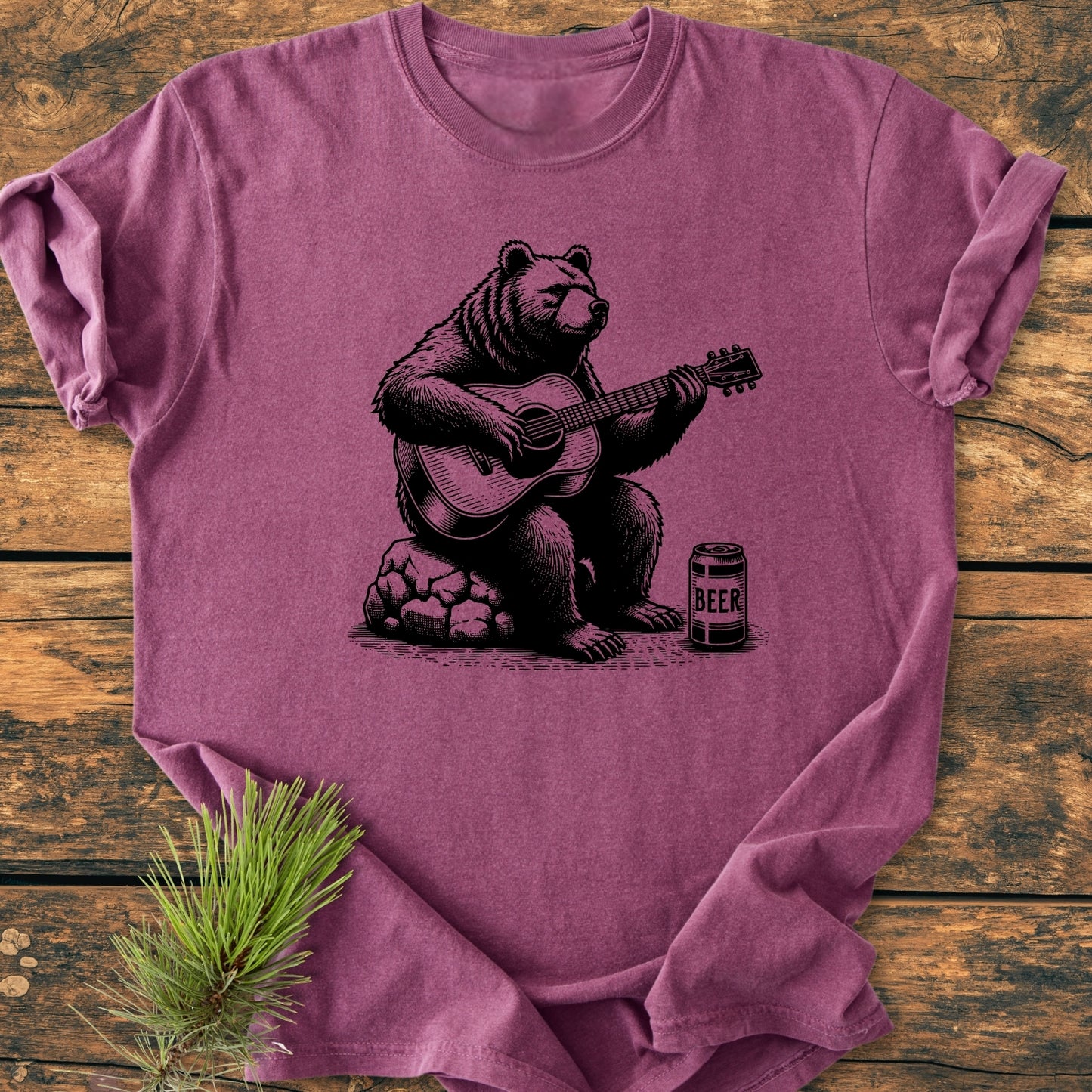 Bear Playing Guitar - Vintage Wash Tee, featuring a bear illustration with a guitar and beer, is displayed on a rustic surface. The heathered plum T-shirt offers a relaxed fit and durable stitching.