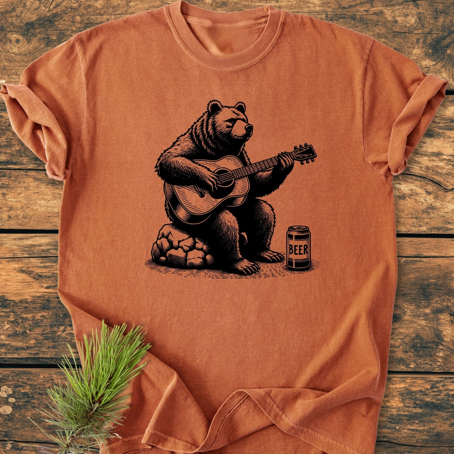 Bear Playing Guitar - Vintage Wash Tee features a black bear graphic strumming a guitar next to a beer can on a rust-orange T-shirt, laid flat with casually rolled sleeves.