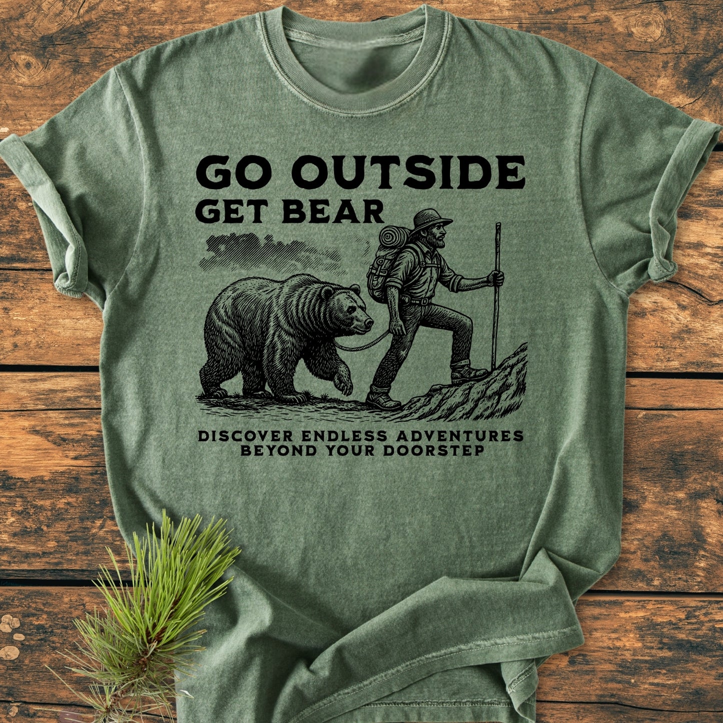 Go Outside Get Bear - Vintage Wash Tee featuring a bearded hiker illustration with a bear, slogan promoting adventure. Displayed on rustic wood with pine sprig, showcasing its relaxed, durable, and cozy design.