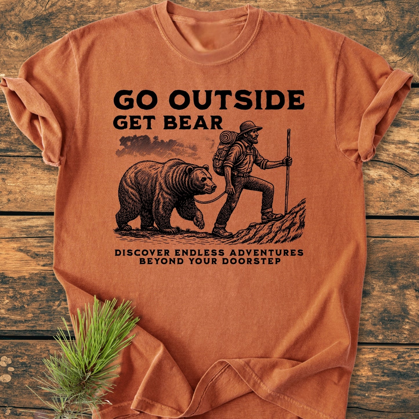 Go Outside Get Bear - Vintage Wash Tee features a bearded hiker with a bear on a leash, promoting adventure with the text DISCOVER ENDLESS ADVENTURES BEYOND YOUR DOORSTEP on a cozy, ring-spun cotton shirt.