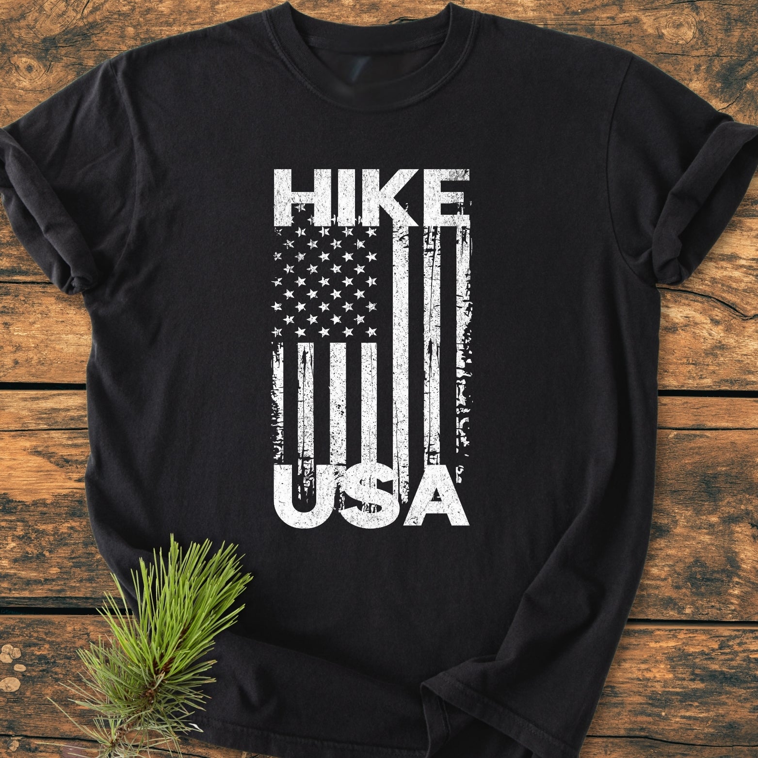Hike USA - Vintage Wash Tee: Black T-shirt on wooden surface, featuring distressed white print of American flag motif with HIKE and USA. Soft, cozy, garment-dyed, relaxed fit, 100% ring-spun cotton.