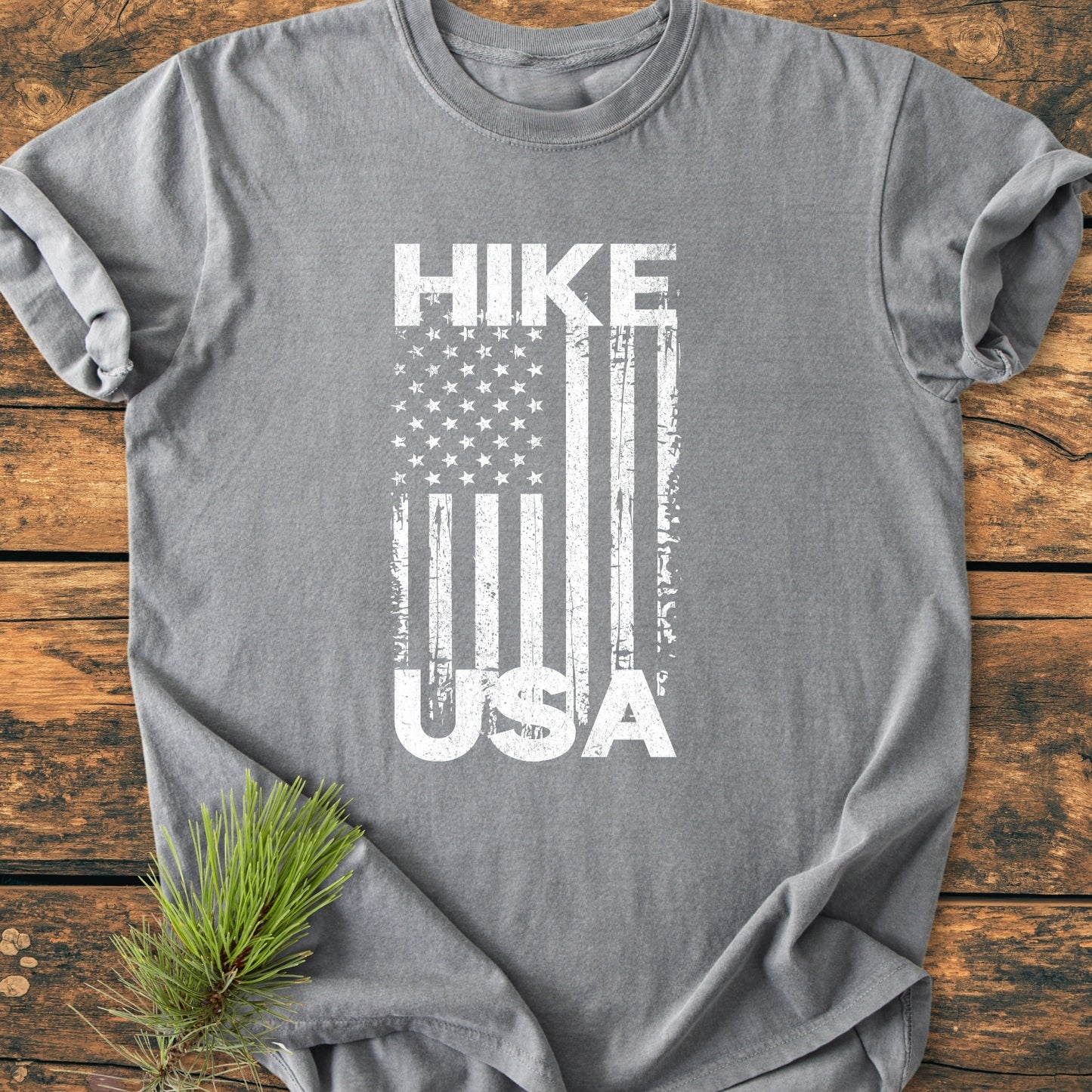 Heather-gray Hike USA - Vintage Wash Tee with distressed American flag design, laid on wood. Features soft-washed, ring-spun cotton, relaxed fit, and durable double-needle stitching. Pine bough accentuates rustic appeal.