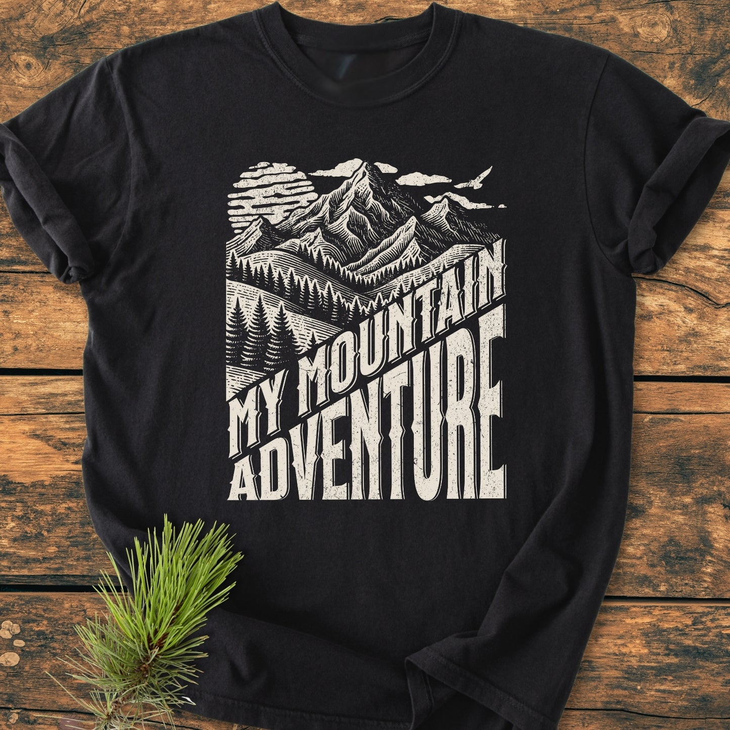 Black My Mountain Adventure - Vintage Wash Tee featuring a vintage-style mountain illustration with a sun and birds, laid on wood. Soft, relaxed fit, perfect for everyday wear.